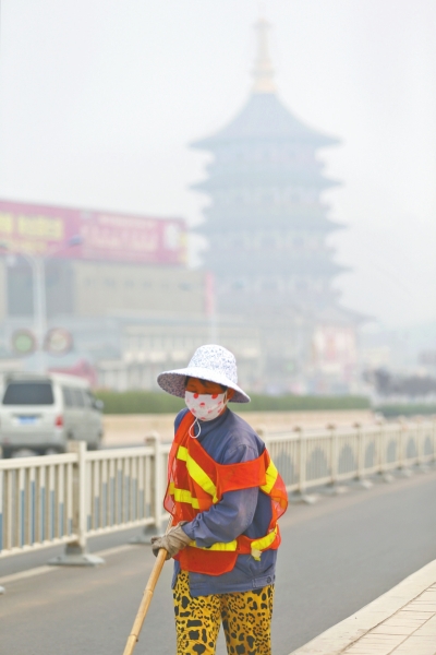 近日，在古都洛陽(yáng)，環(huán)衛(wèi)工人身后的“天堂”被霧霾籠罩著。