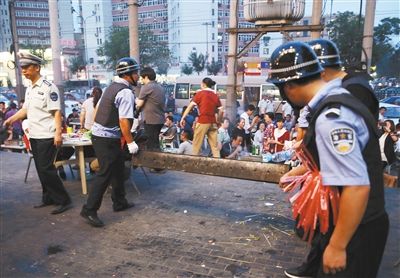 6月13日晚8點，朝陽路和青年路交叉口西側(cè)，一次聯(lián)合執(zhí)法行動中，輔警與協(xié)管抬走商戶的燒烤用具。新京報記者 尹亞飛 攝