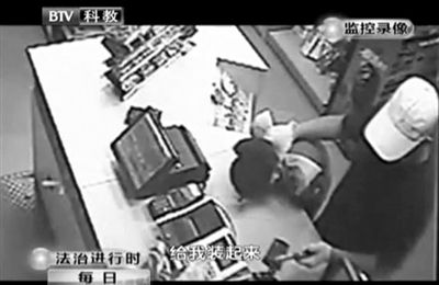 戴帽男子一手掐住加油站營(yíng)業(yè)員，一手持發(fā)令槍指向另一營(yíng)業(yè)員，要求“把錢(qián)給我裝起來(lái)”。