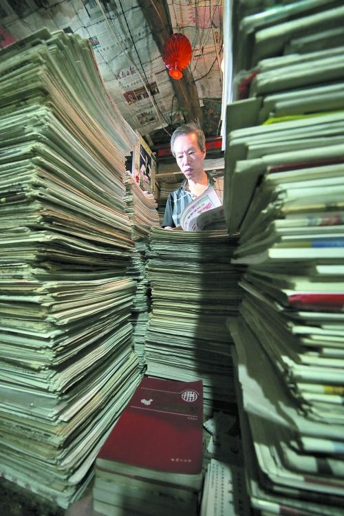 王曉民坐在寫(xiě)字桌前，被報(bào)紙淹沒(méi)。