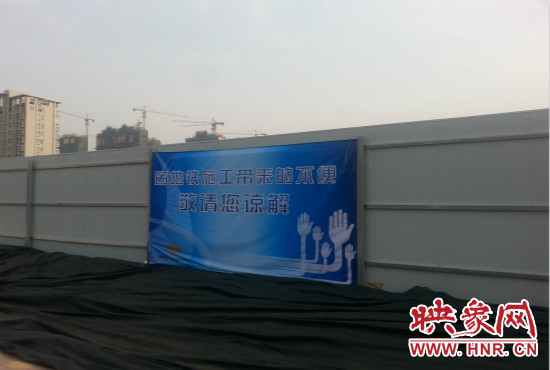 道路南側(cè)圍起了白色的圍擋，墻上標(biāo)示著“因地鐵施工帶來的不便敬請您諒解”的提示牌。